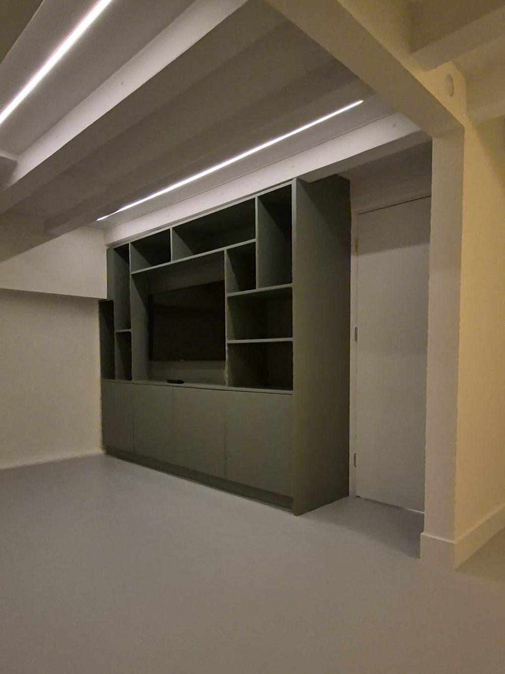 Souterrain met een groene inbouwkast met open vakken rond een tv-nis en ledstrips tussen witte plafondbalken in Oud-Zuid.