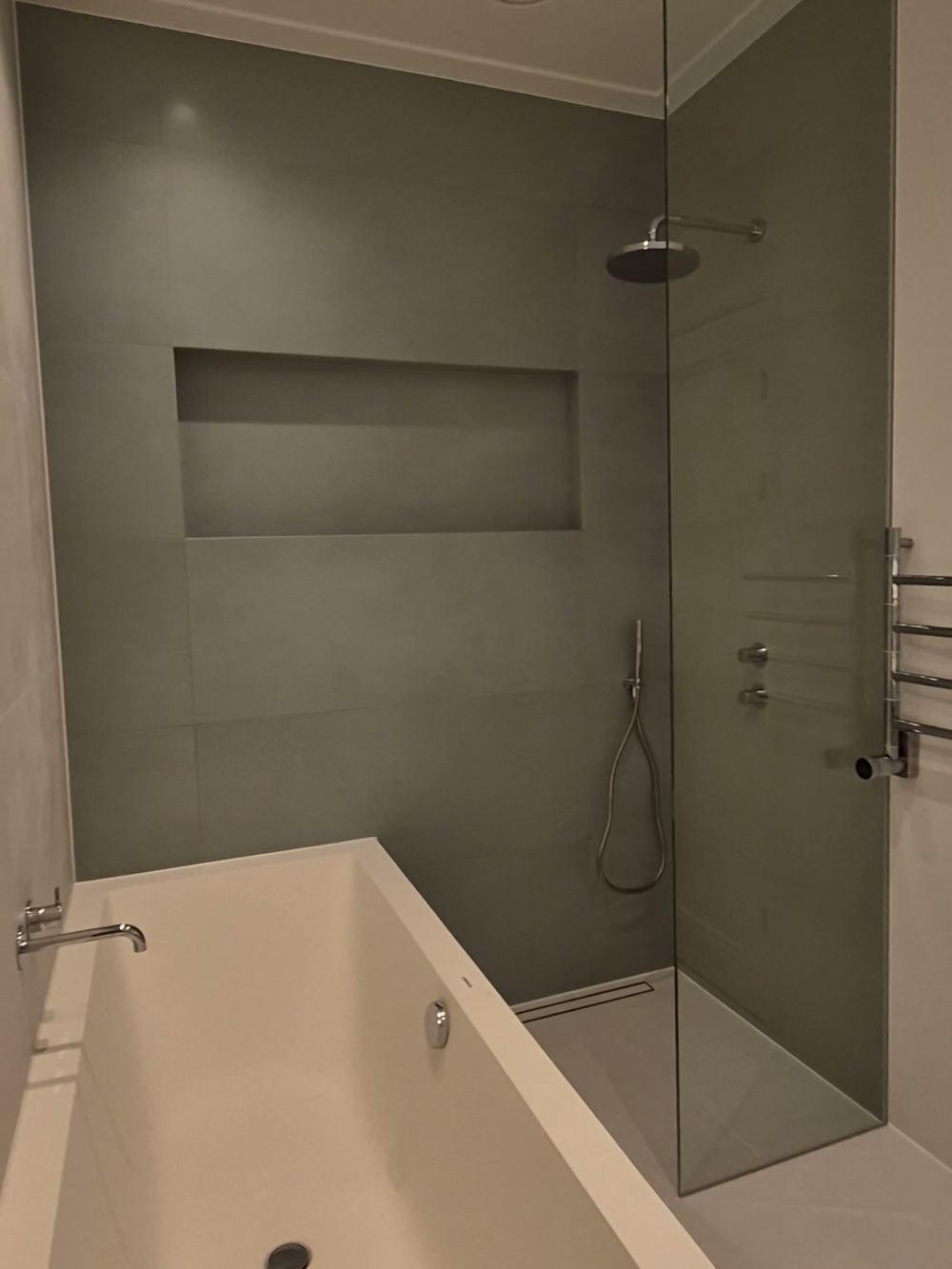 Badkamer met een ingebouwd bad, een inloopdouche achter een glazen wand, een lange wandnis, een regendouche en een verchroomde handdoekradiator in De Pijp.