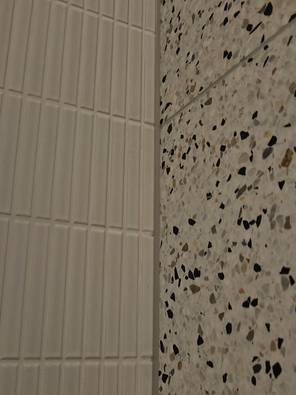 Detail van witte staande staafjestegels naast gespikkelde tegels met terrazzopatroon in een badkamer in De Pijp.