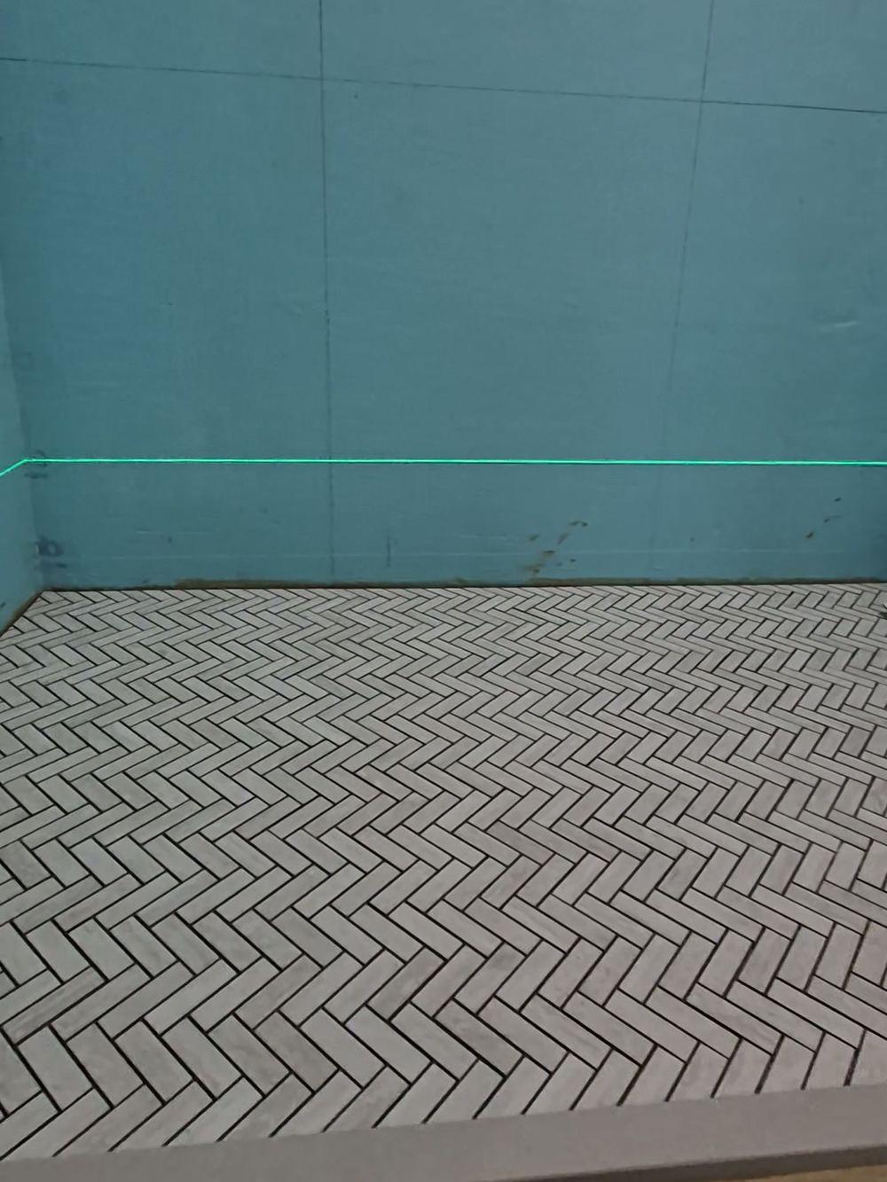 Witte visgraatmozaïek op een douchevloer tussen turquoise gecoate wanden, met een groene laserlijn voor het tegelwerk, in Oud-Zuid (in uitvoering).