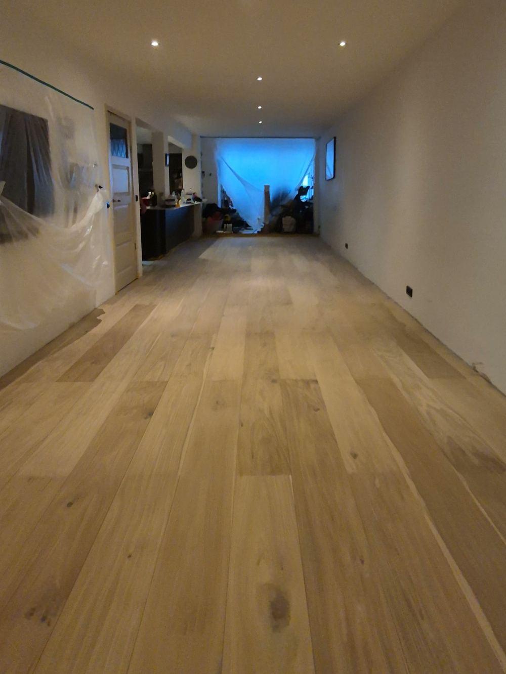 Lange kamer met een nieuw gelegde vloer van brede planken en inbouwspots in een pand in de Jordaan.