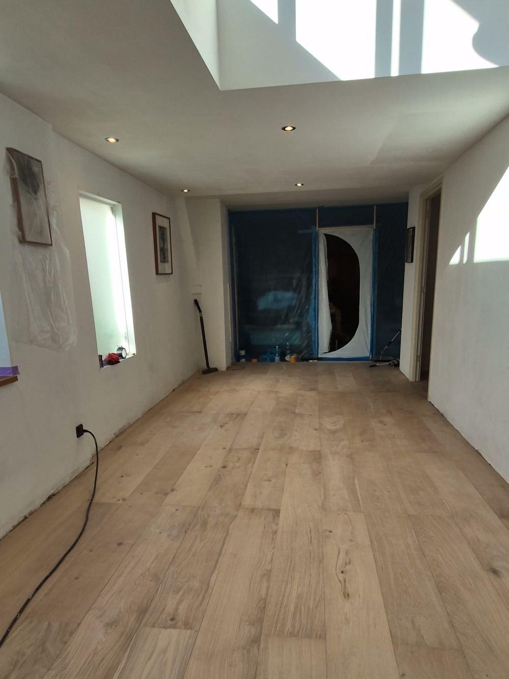 Lange kamer onder een daklicht met een nieuw gelegde vloer van brede planken en ramen in de zijmuur in de Jordaan.