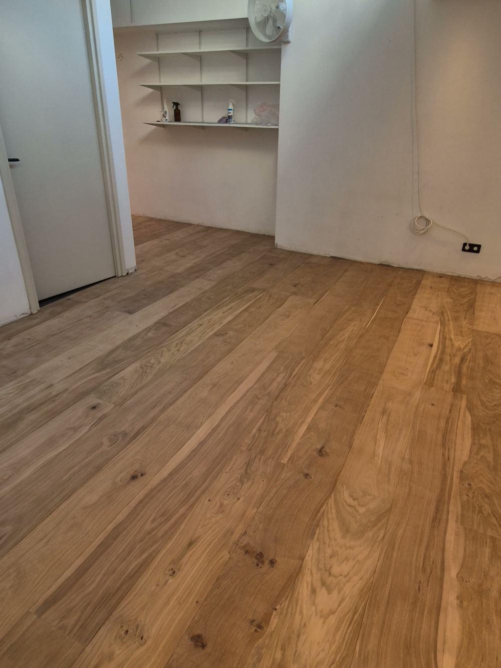 Zonnige kamer met een nieuw gelegde vloer van brede planken, witte wandplanken en een open deur in de Jordaan.