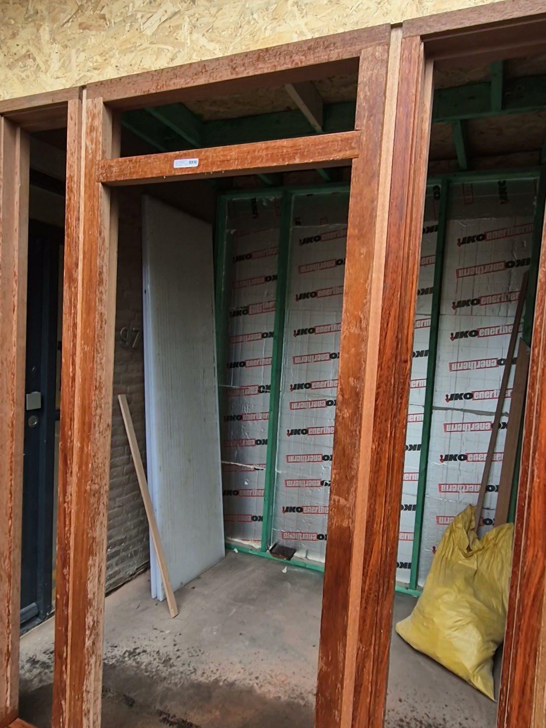 Binnen in de entreeaanbouw: hardhouten kozijnen voor een raam en een deur, een geïsoleerde houtskeletwand en een OSB-plafond (in uitvoering).