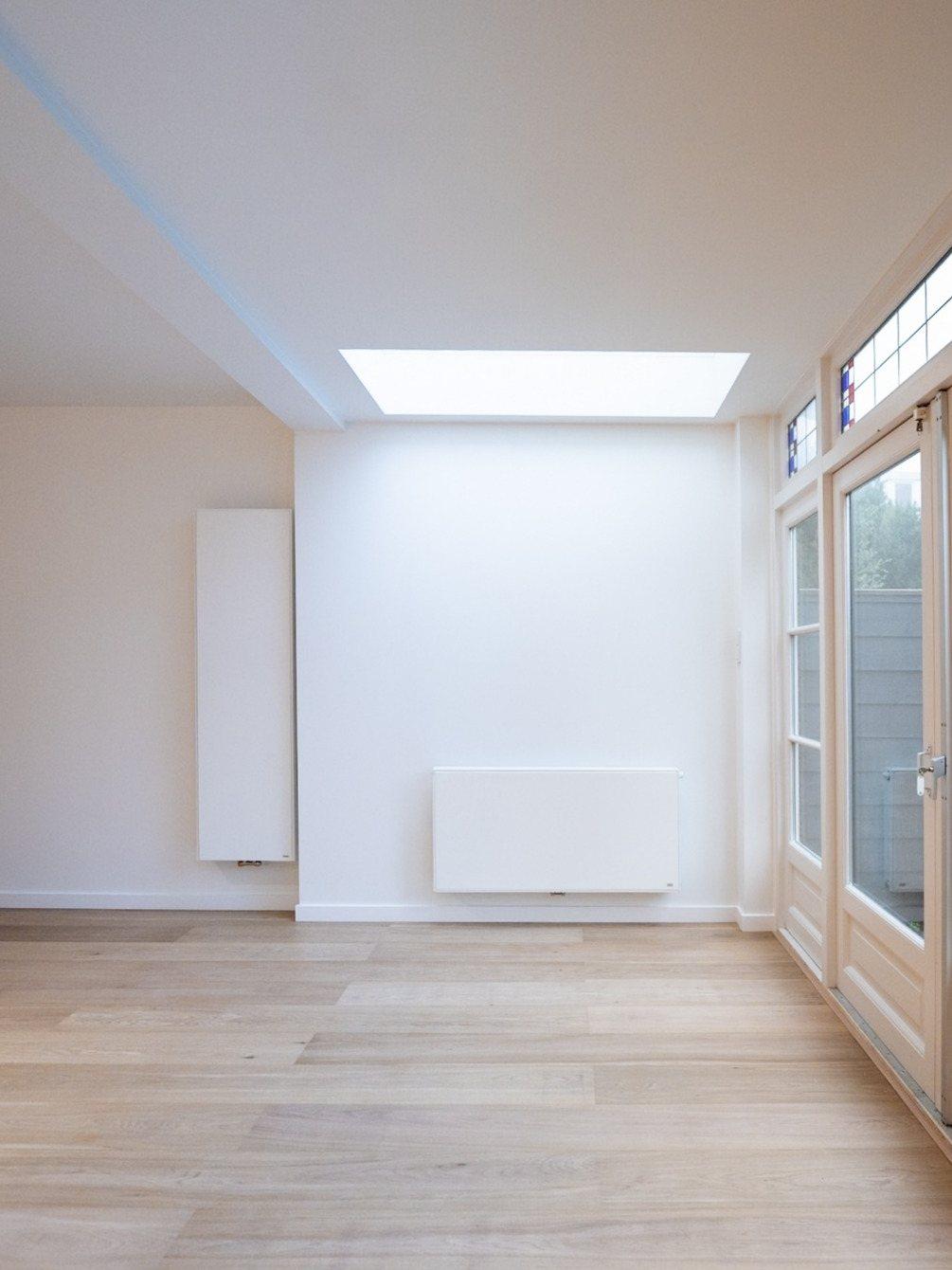 Afgewerkte uitbouw in Amstelveen: een lichte ruimte met daklicht, witte wanden, radiatoren, tuindeuren en een lichte houten vloer.