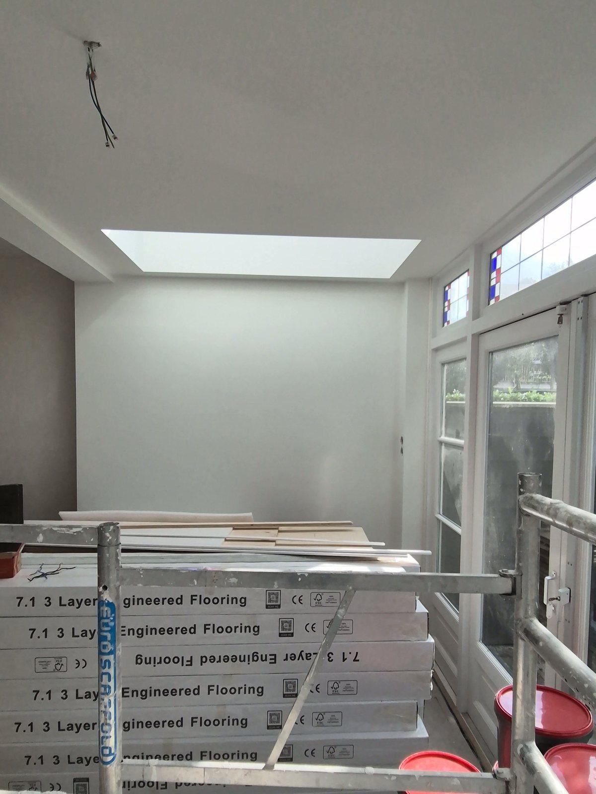 Uitbouw voordat de vloer erin komt: gestucte wanden, een daklicht, tuindeuren met glas-in-lood bovenlichten, dozen met houten vloerdelen en een steiger (in uitvoering).