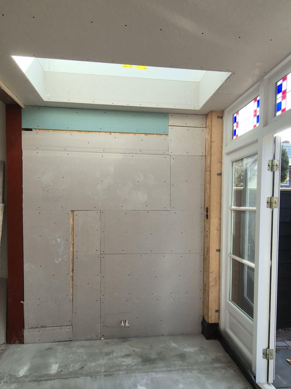 Nieuw daklicht boven beplaatte wanden, een roodgegronde stalen kolom en tuindeuren met glas-in-lood bovenlichten in een uitbouw (in uitvoering).