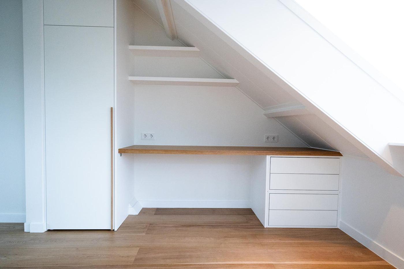 Built-in desk with drawers and shelves in a niche under the roof slope, next to a tall white wardrobe.