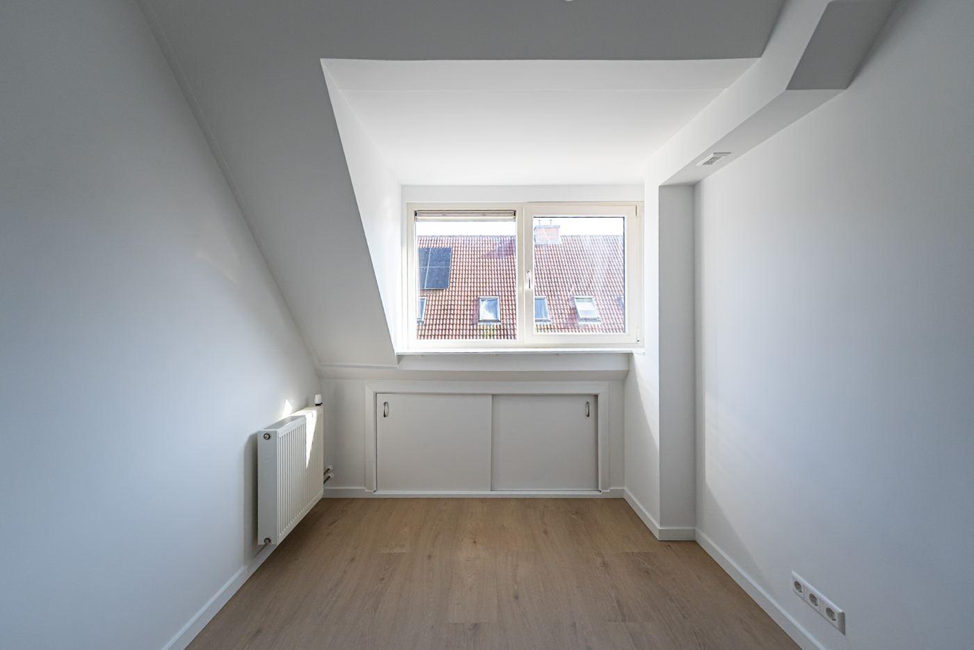 Small attic room with a dormer window, sliding cupboard doors under the window and a wood-look floor.