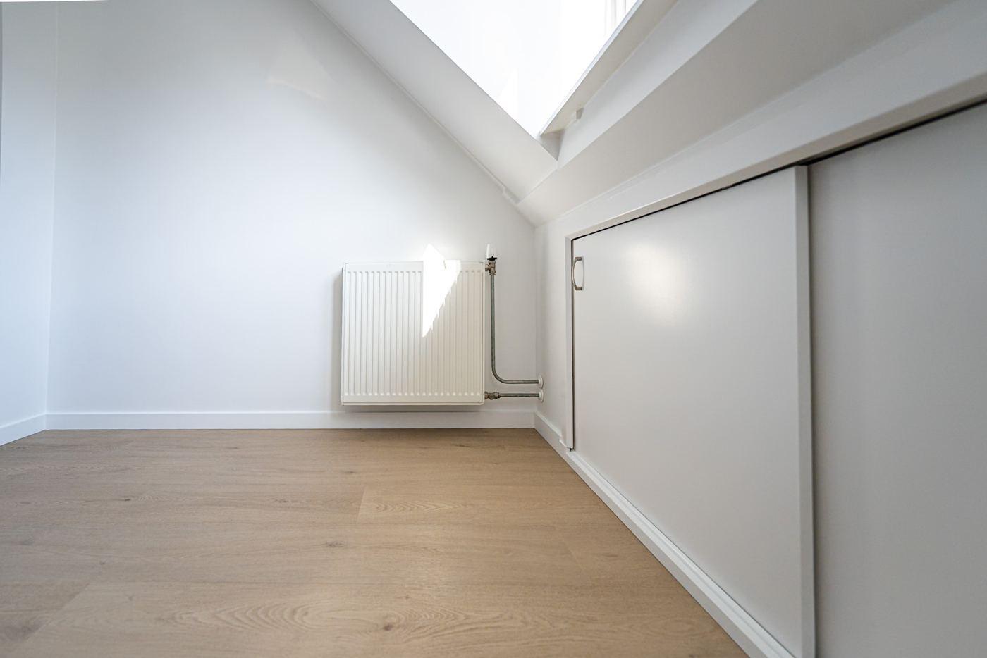 Attic room with sliding doors to storage space in the knee wall under the roof slope, a radiator and a wood-look floor.