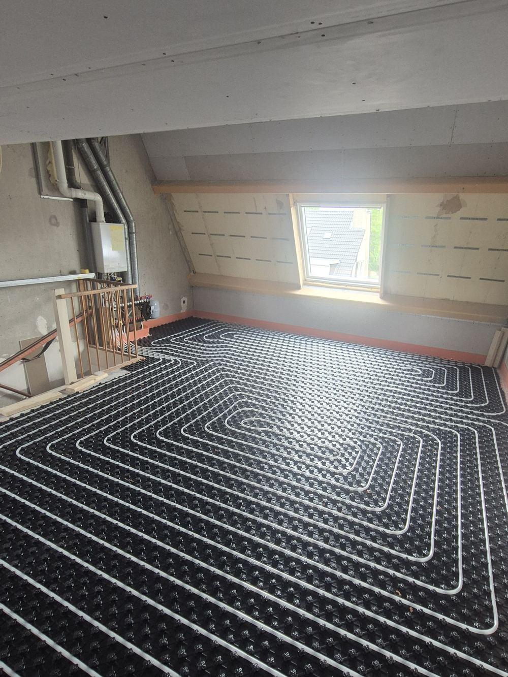 Attic floor with underfloor heating pipes laid out, a stair opening with a railing and a small window (in progress).