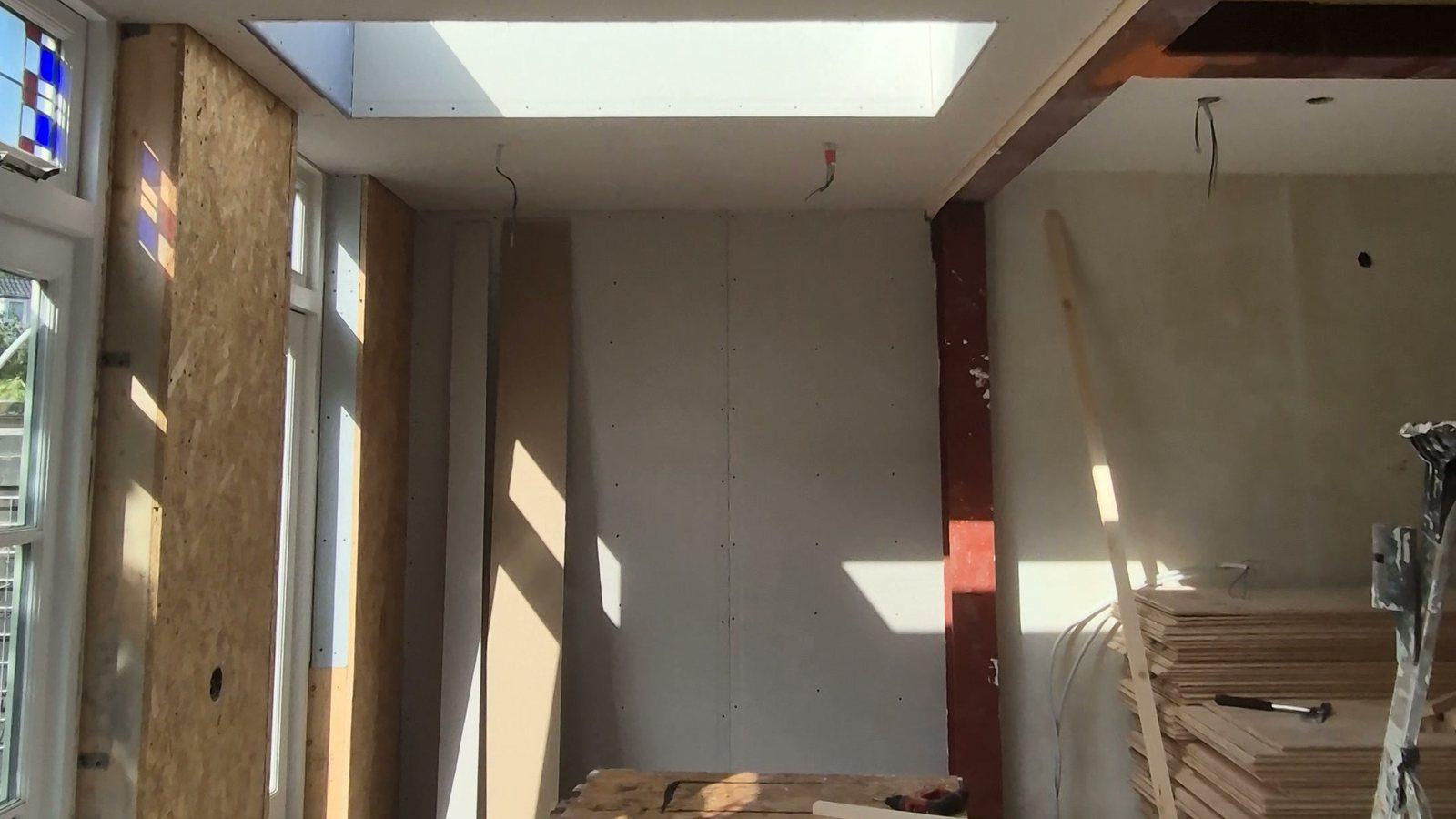 Uitbouw in aanbouw: een daklicht in het nieuwe plafond, een roodgegronde stalen kolom en balk bij de geopende oude achtergevel, OSB-wanden en glas-in-lood bovenlichten