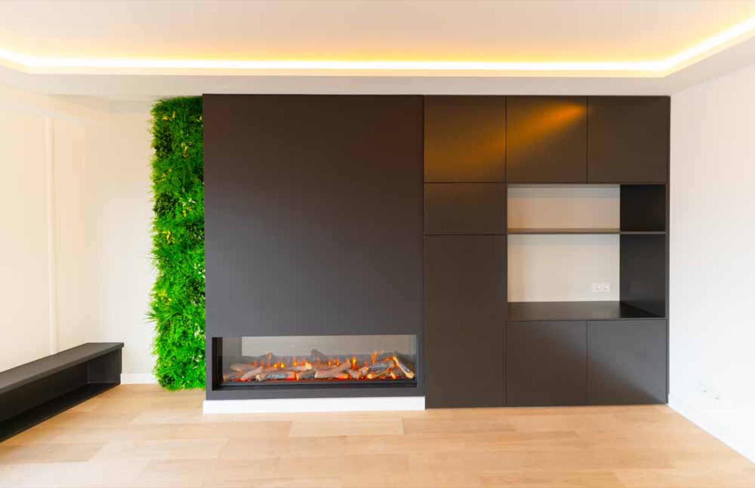 Renovated living room with a dark built-in cabinet wall, an electric fireplace, a moss wall panel, cove lighting in the ceiling and an oak floor